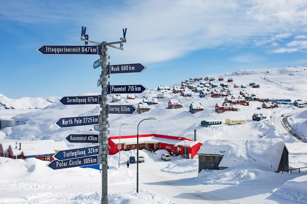 Cartello informativo con distanze e vista su Tasiilaq in inverno